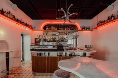 Stylowy bar z neonowym oświetleniem, metalowymi detaliami i marmurowym blatem.