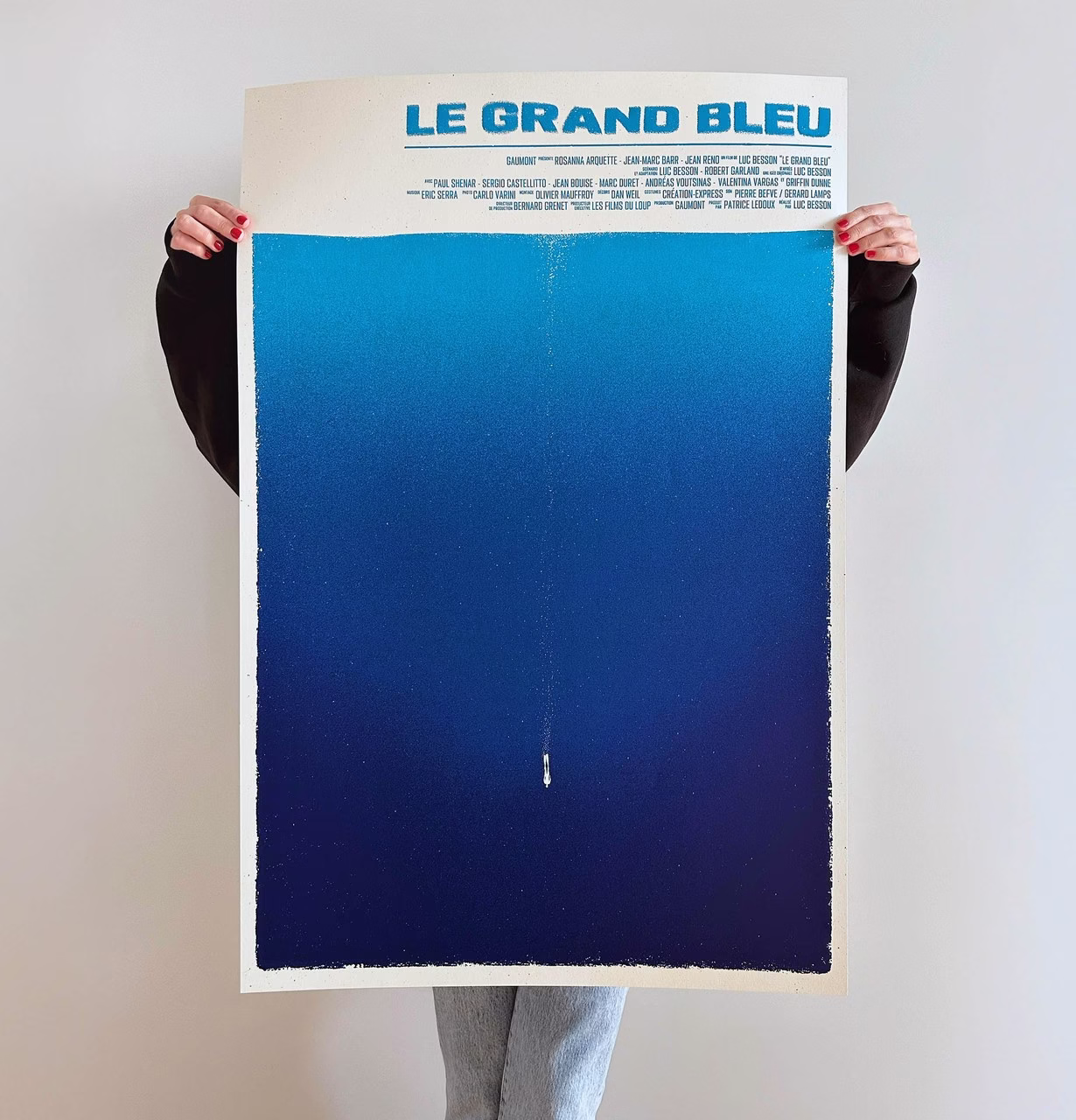 Osoba trzymająca plakat filmu Le Grand Bleu z niebieskim gradientem.