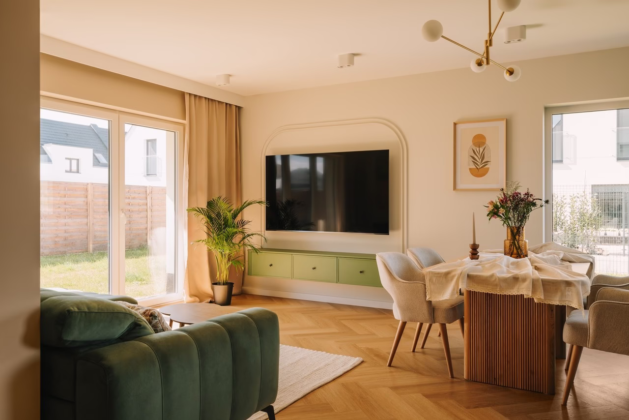 Jasny salon z elegancką sofą, zielonymi akcentami i drewnianą podłogą.