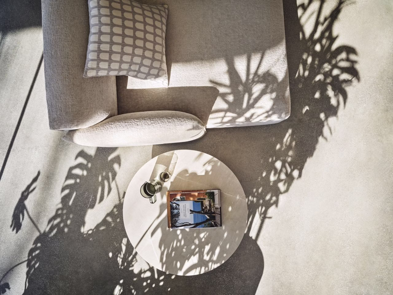 Beżowa sofa, okrągły stolik, cienie monstery, elegancki magazyn, minimalistyczny design.