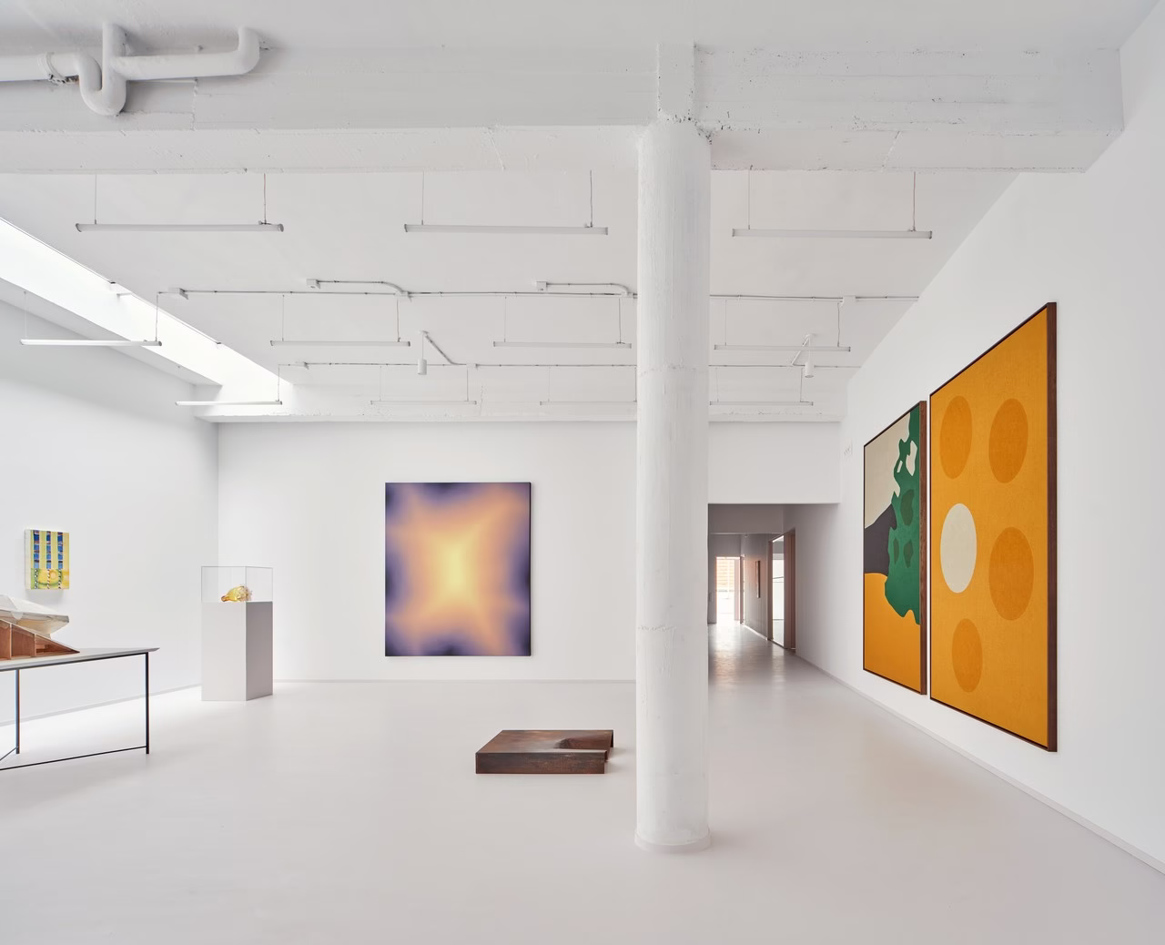 Minimalistyczna galeria sztuki z dużymi kolorowymi obrazami na białych ścianach.