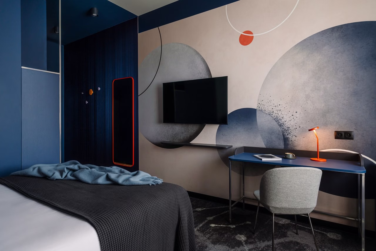 Stylowy pokój hotelowy z abstrakcyjną tapetą i niebieskimi akcentami.