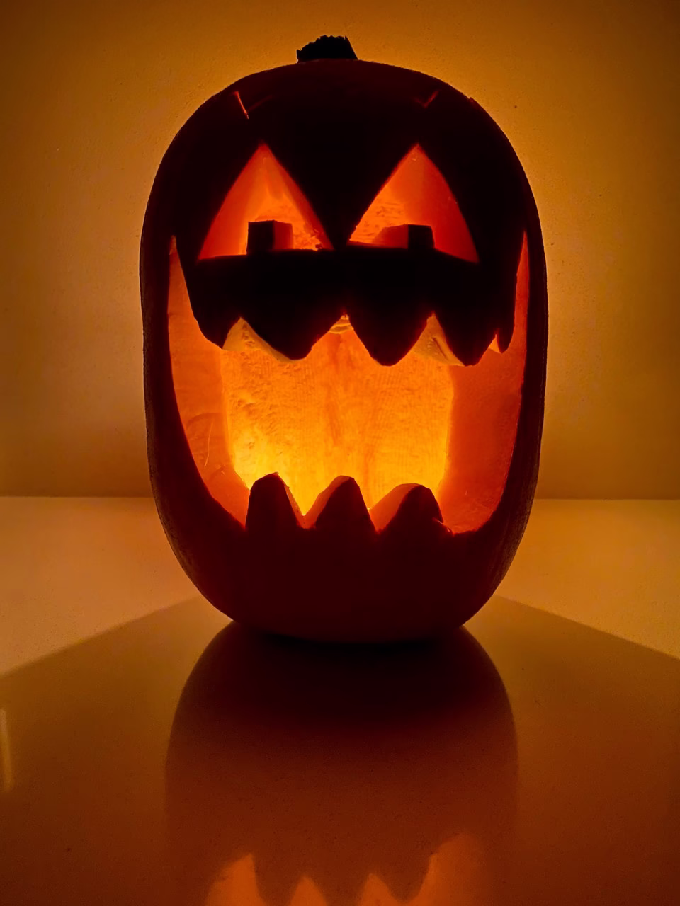 Podświetlona dynia Halloween z wyciętym uśmiechem na tle ciemności.