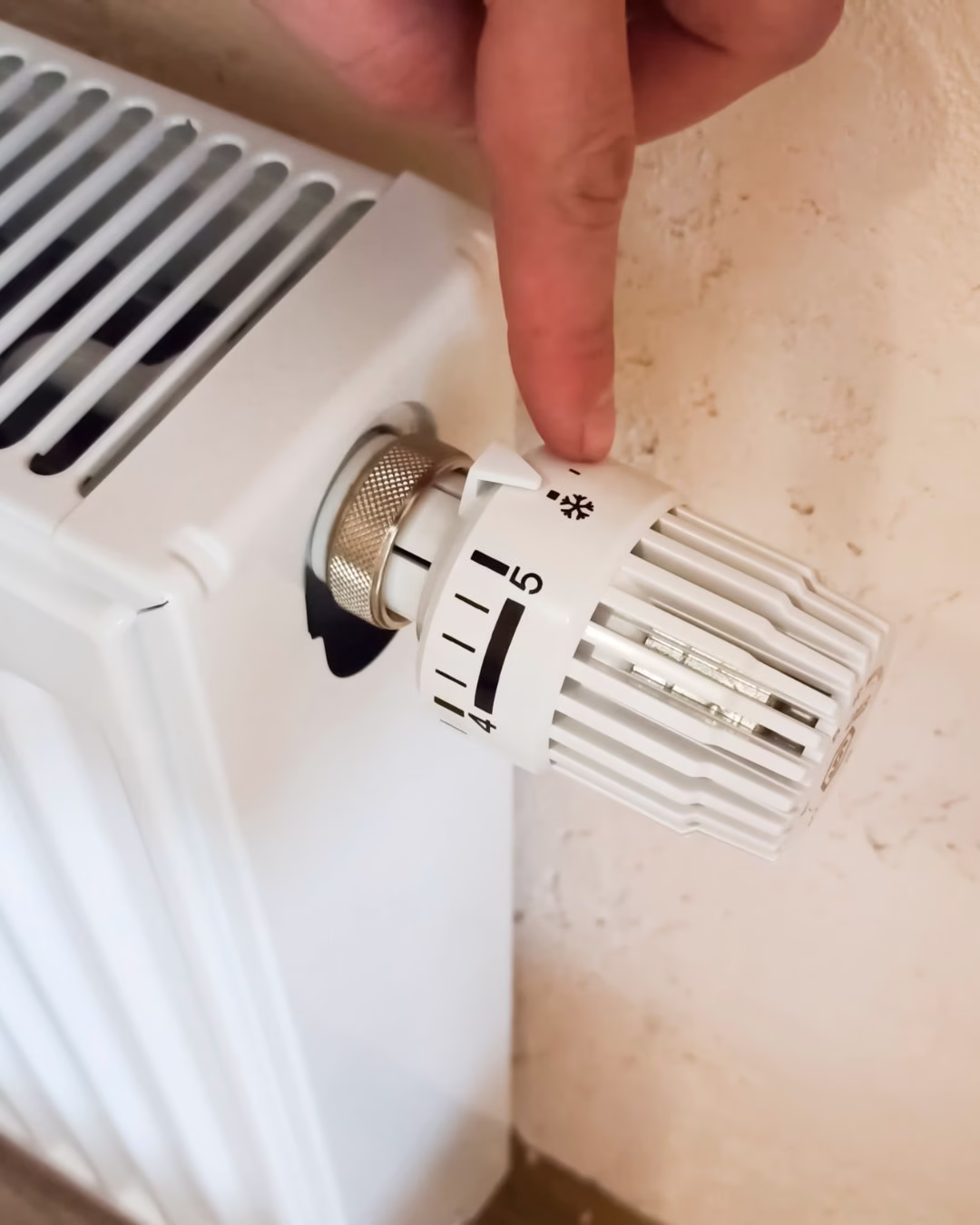 Palec zmienia temperaturę na białym kaloryferze z pokrętłem termostatycznym.