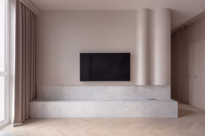 Minimalistyczny salon z beżowymi ścianami, telewizorem i drewnianą podłogą.