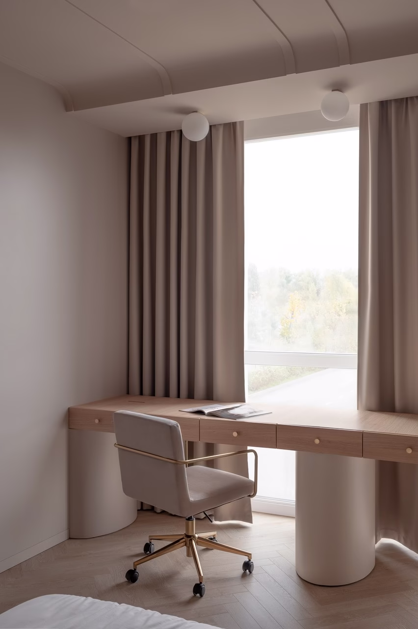 Nowoczesne biurko z jasnego drewna, beżowy fotel, minimalistyczne zasłony.
