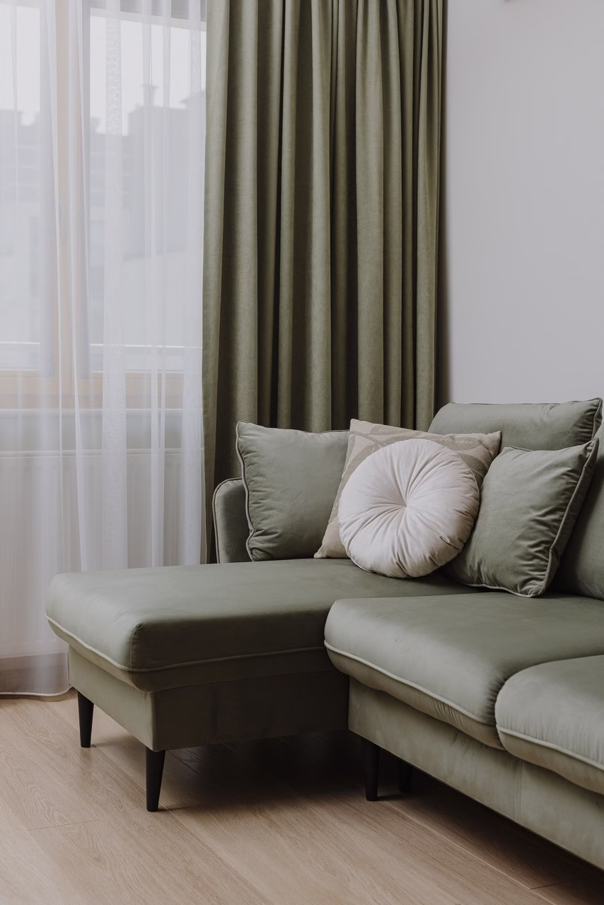 Minimalistyczny salon z zieloną sofą i beżowymi poduszkami, drewniana podłoga.