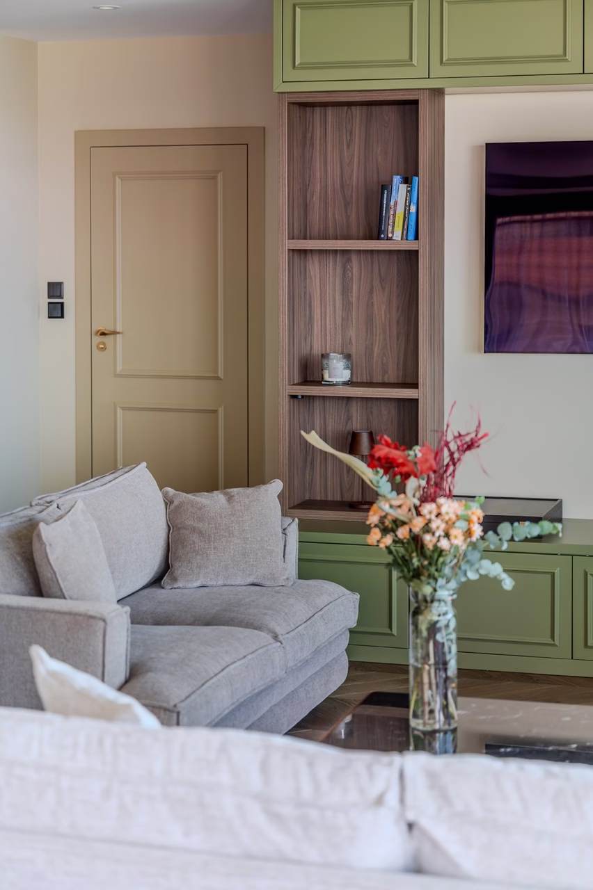 Nowoczesny salon z zielonymi szafkami, beżową sofą i kwiatami w wazonie.