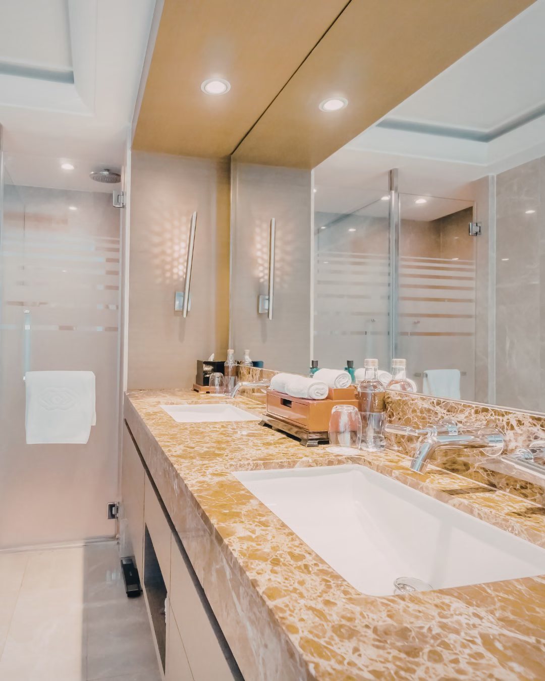 Luksusowa łazienka z marmurowym blatem, podwójną umywalką i szklanym prysznicem.