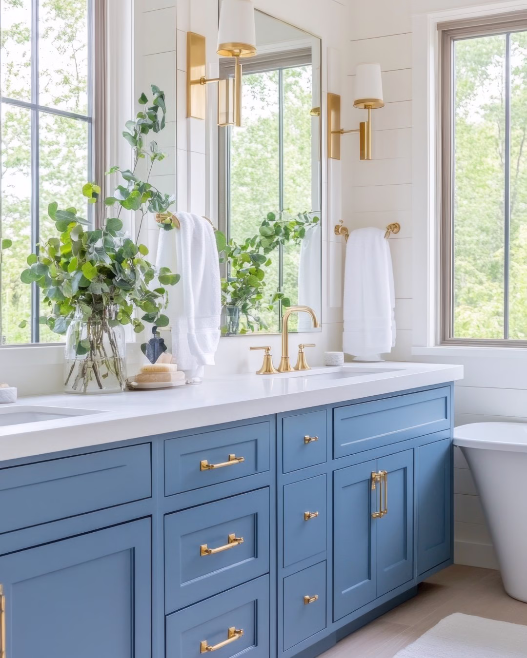 Elegancka łazienka z niebieską szafką, złotymi uchwytami i roślinami.