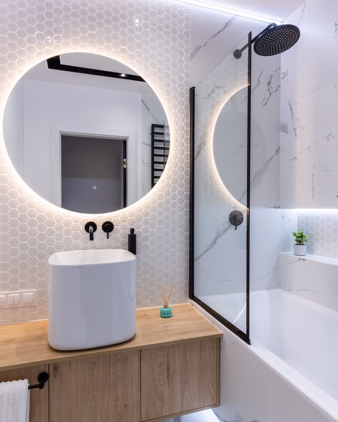 Nowoczesna łazienka z oświetlonym lustrem, drewnianą szafką i heksagonalnymi płytkami.