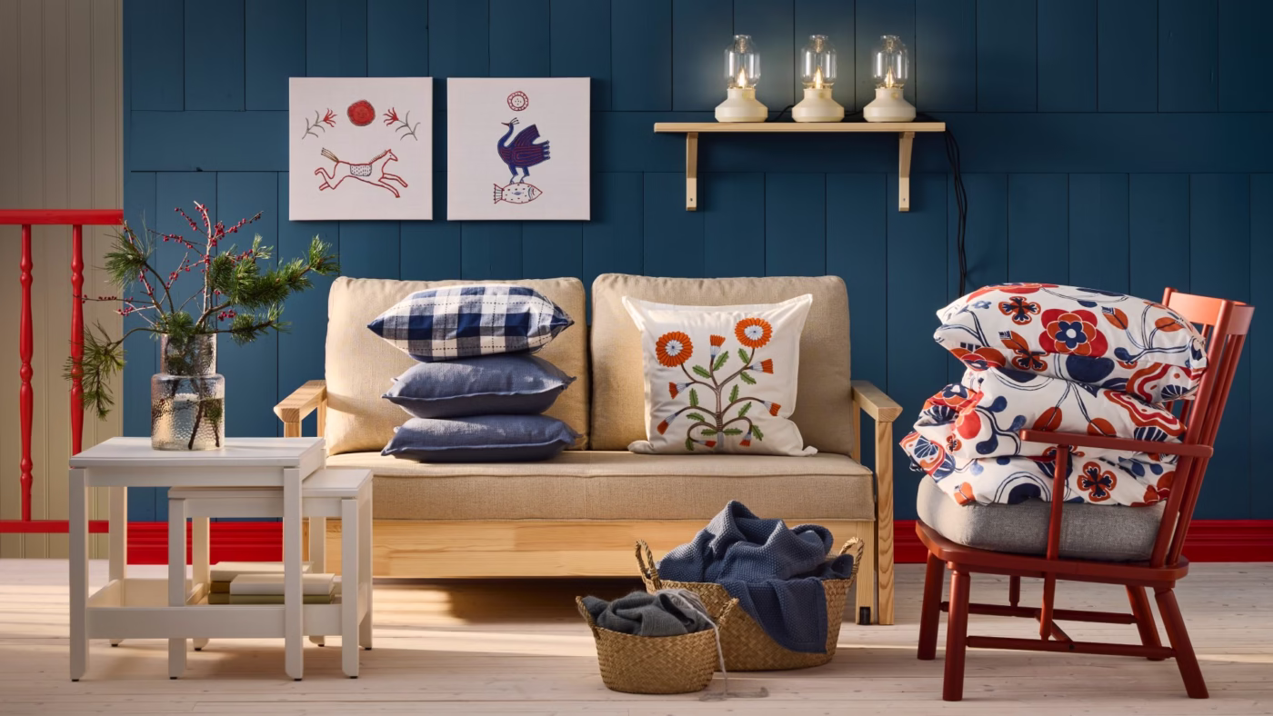 Beżowa sofa, czerwony fotel, niebieska ściana, poduszki z kwiatami i ptakami.