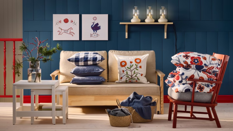 Beżowa sofa, czerwony fotel, niebieska ściana, poduszki z kwiatami i ptakami.