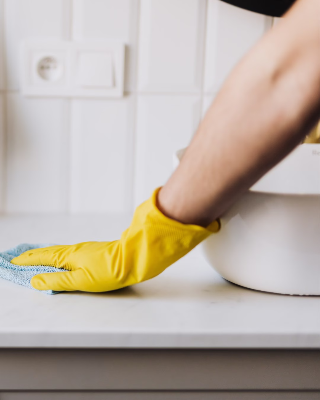Żółta rękawica czyszcząca białą kuchenną ladę niebieską ściereczką.