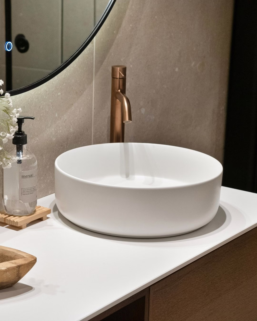 Nowoczesna łazienka z białą umywalką nablatową i złotą baterią.