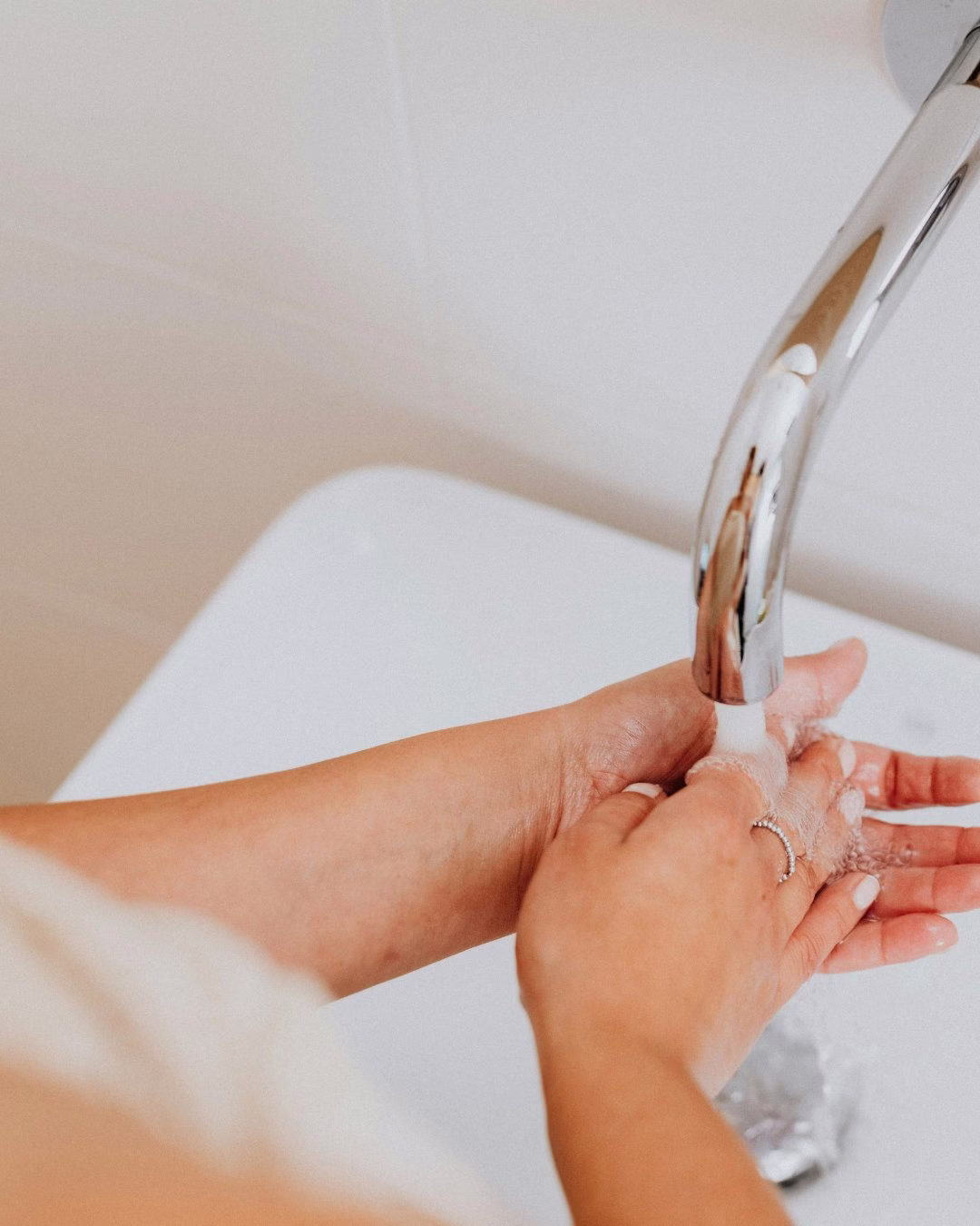 Osoba myjąca ręce pod nowoczesną chromowaną baterią w łazience.