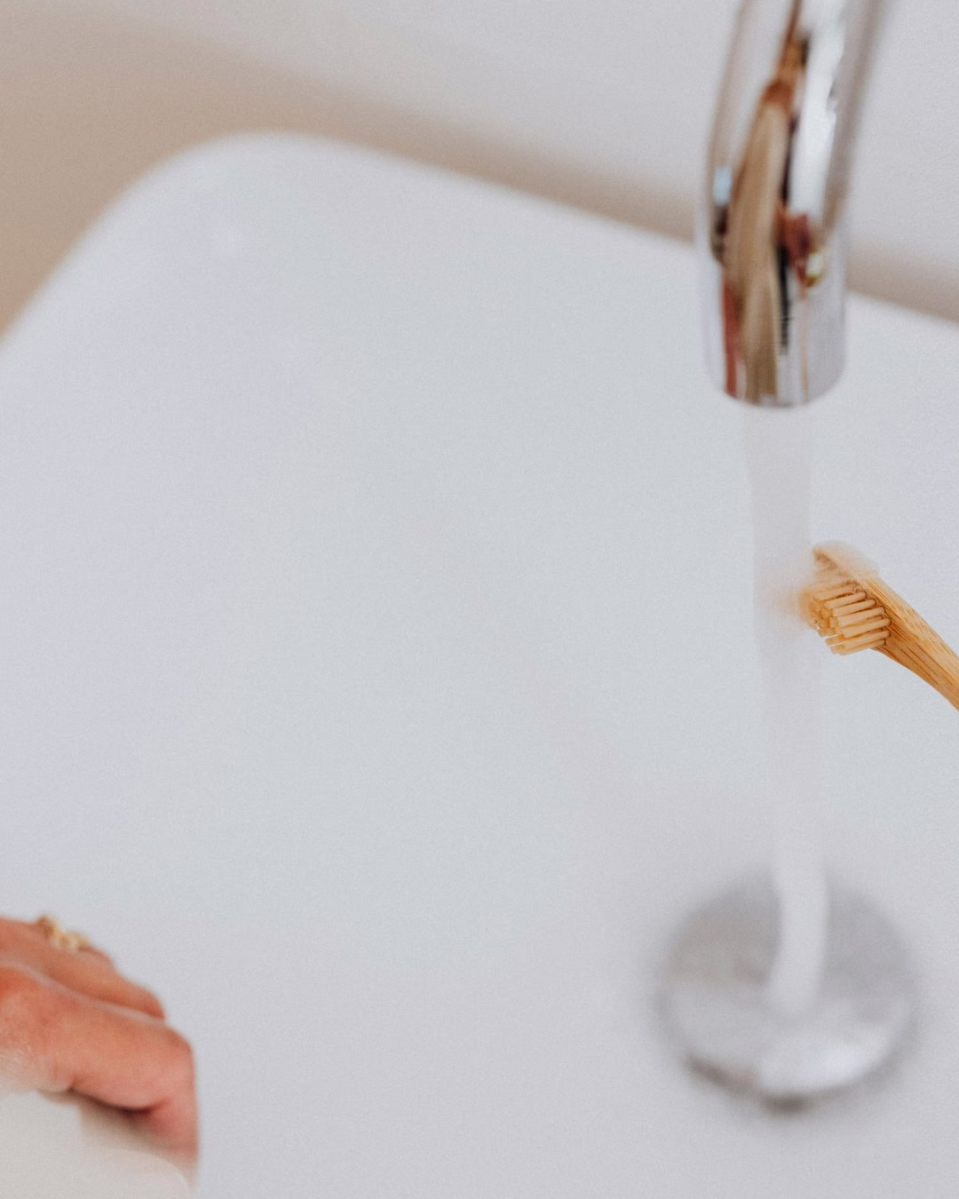 Bambusowa szczoteczka do zębów pod bieżącą wodą z chromowanej baterii.