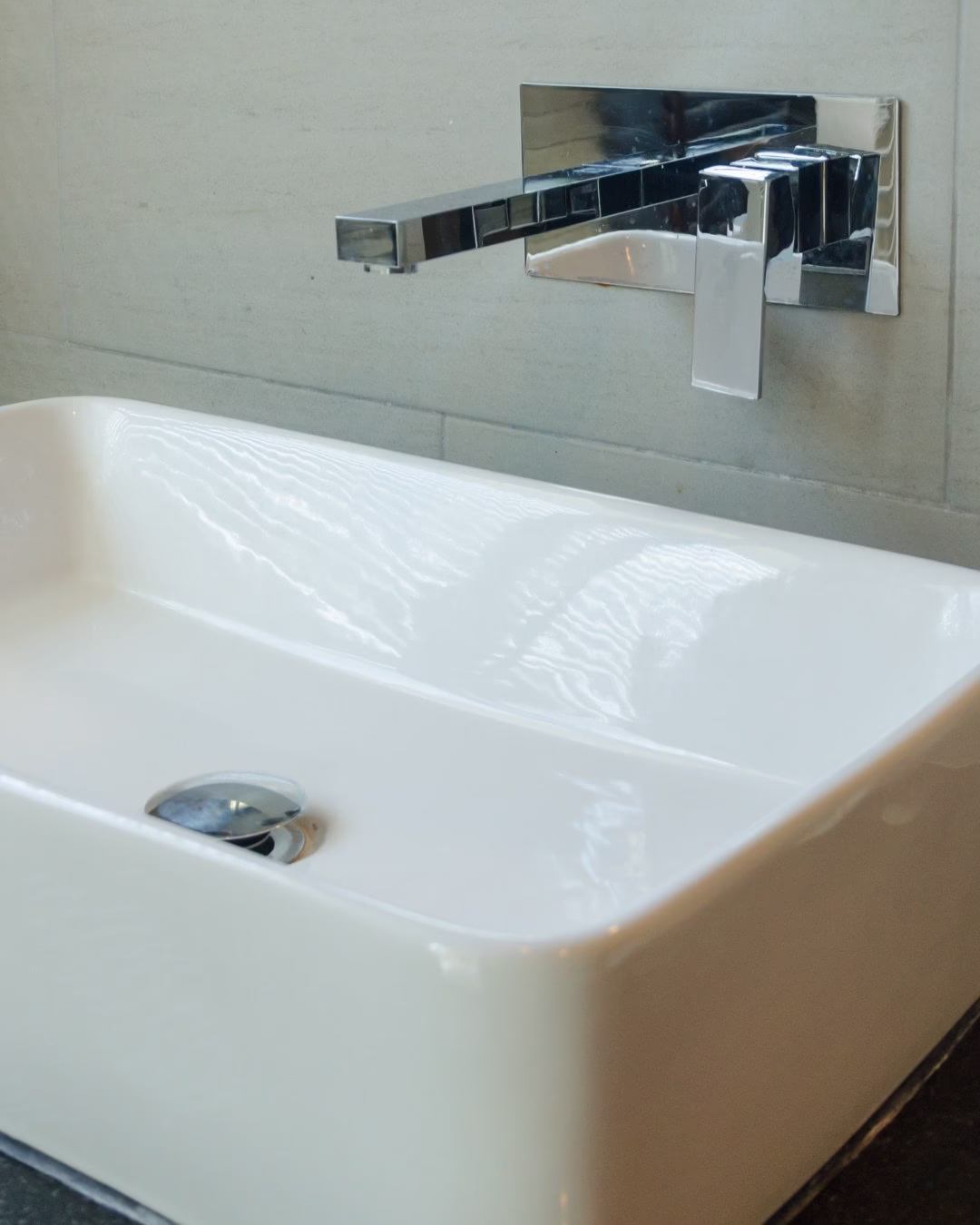 Biały nowoczesny zlew z chromowaną baterią na tle jasnej ściany.