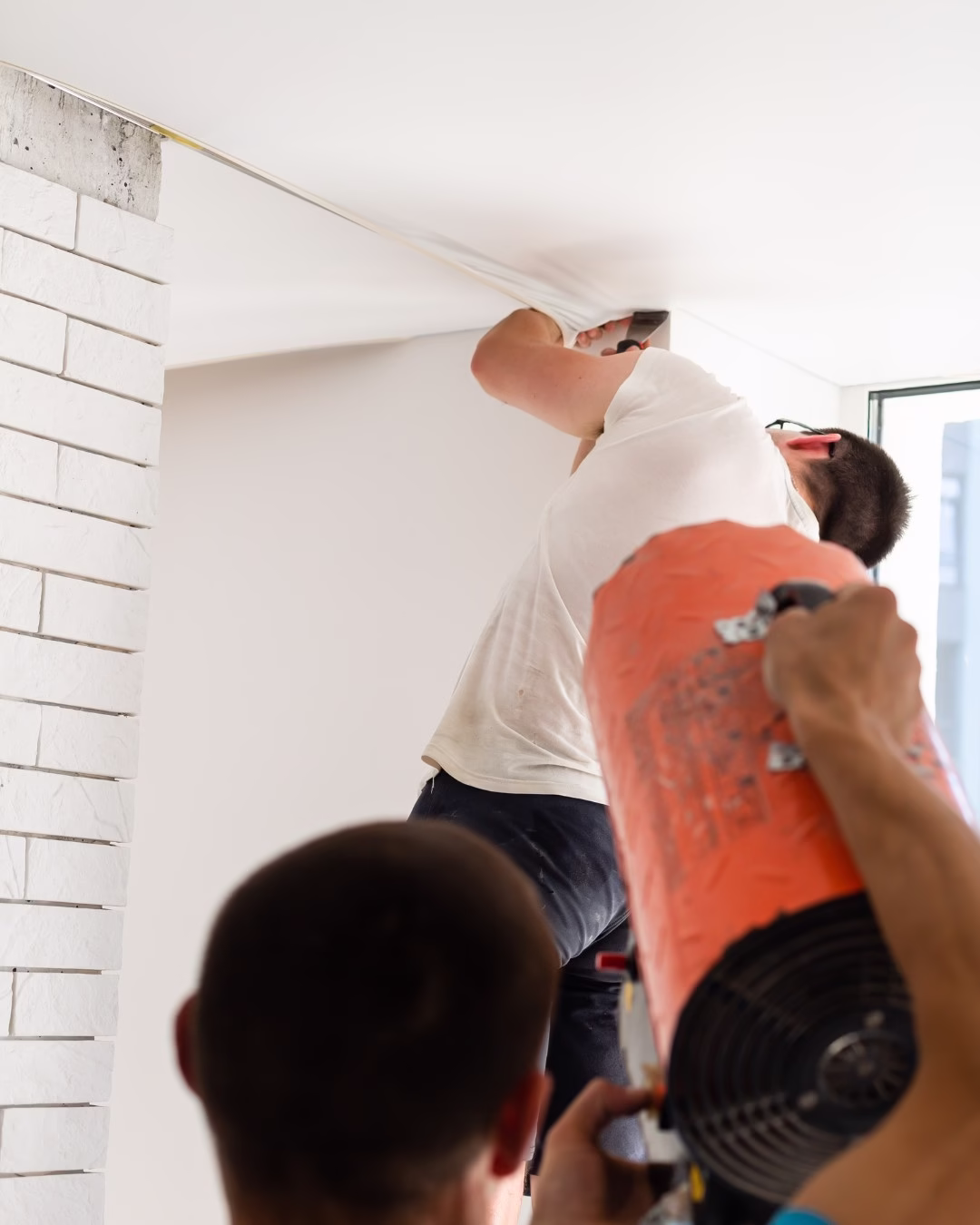 Montaż podsufitki napinanej w nowoczesnym, jasnym wnętrzu z białymi cegłami.