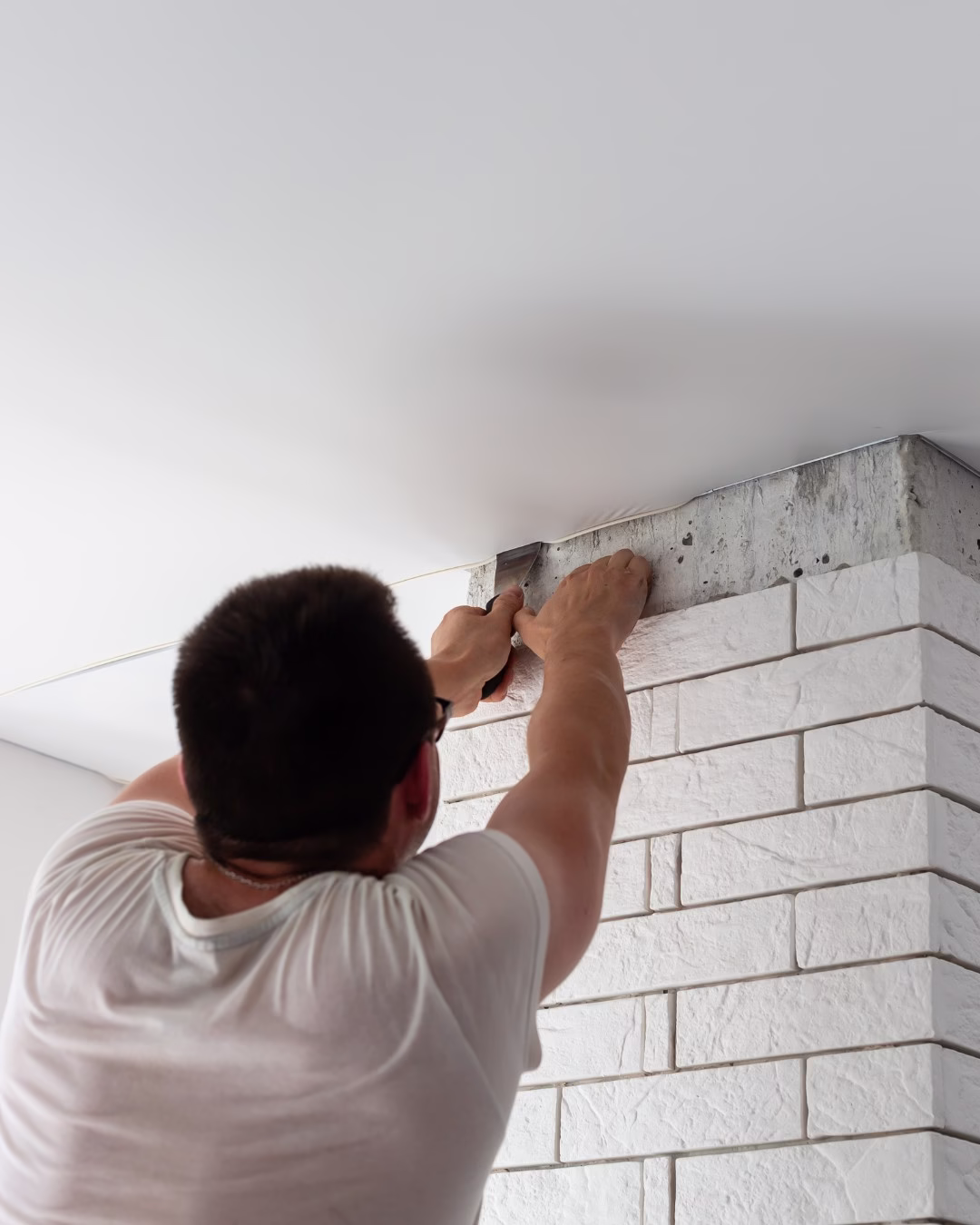 Mężczyzna pracujący nad montażem sufitu przy białych cegłach.