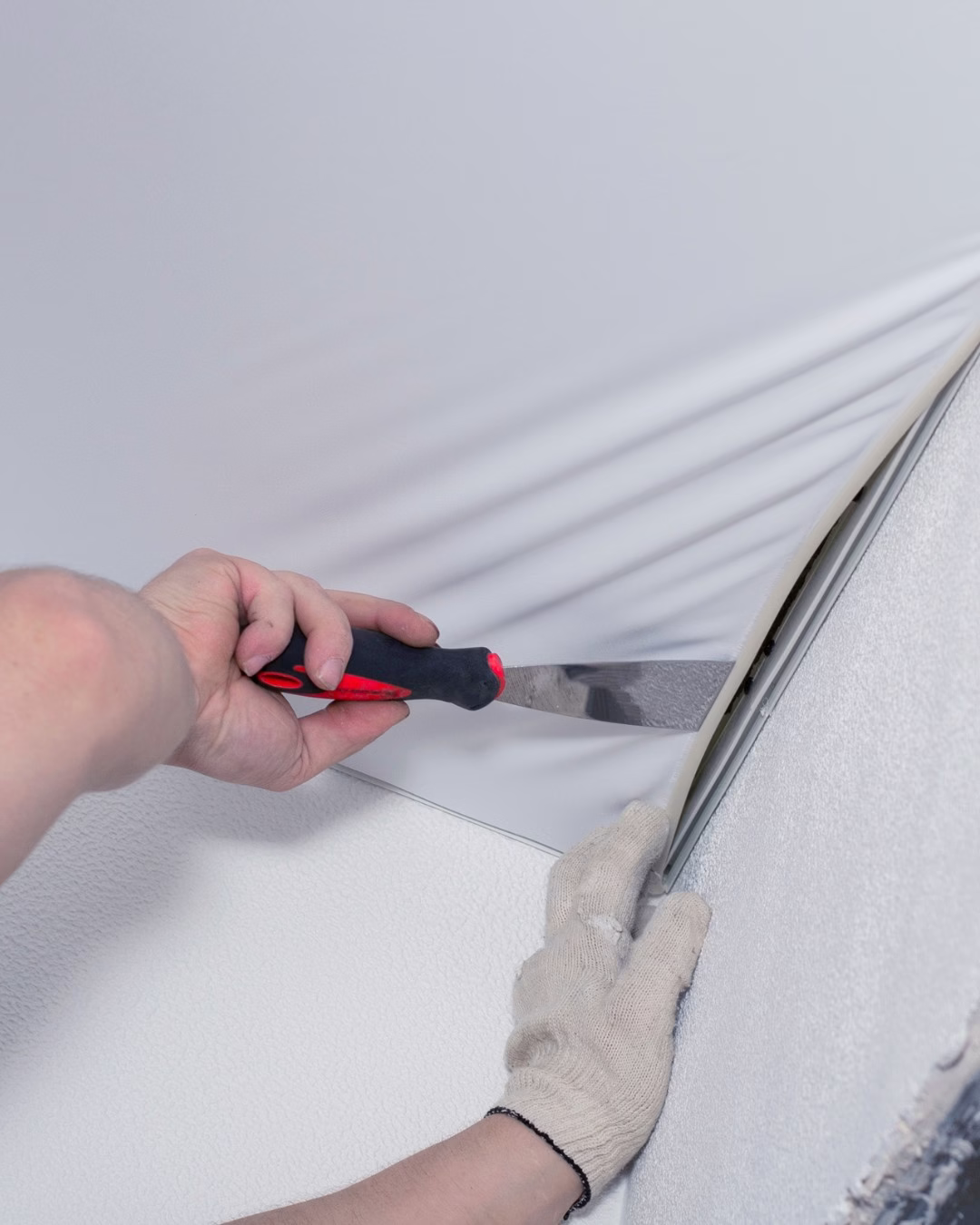 Montaż napinanego sufitu z użyciem szpachelki, białe matowe wykończenie.