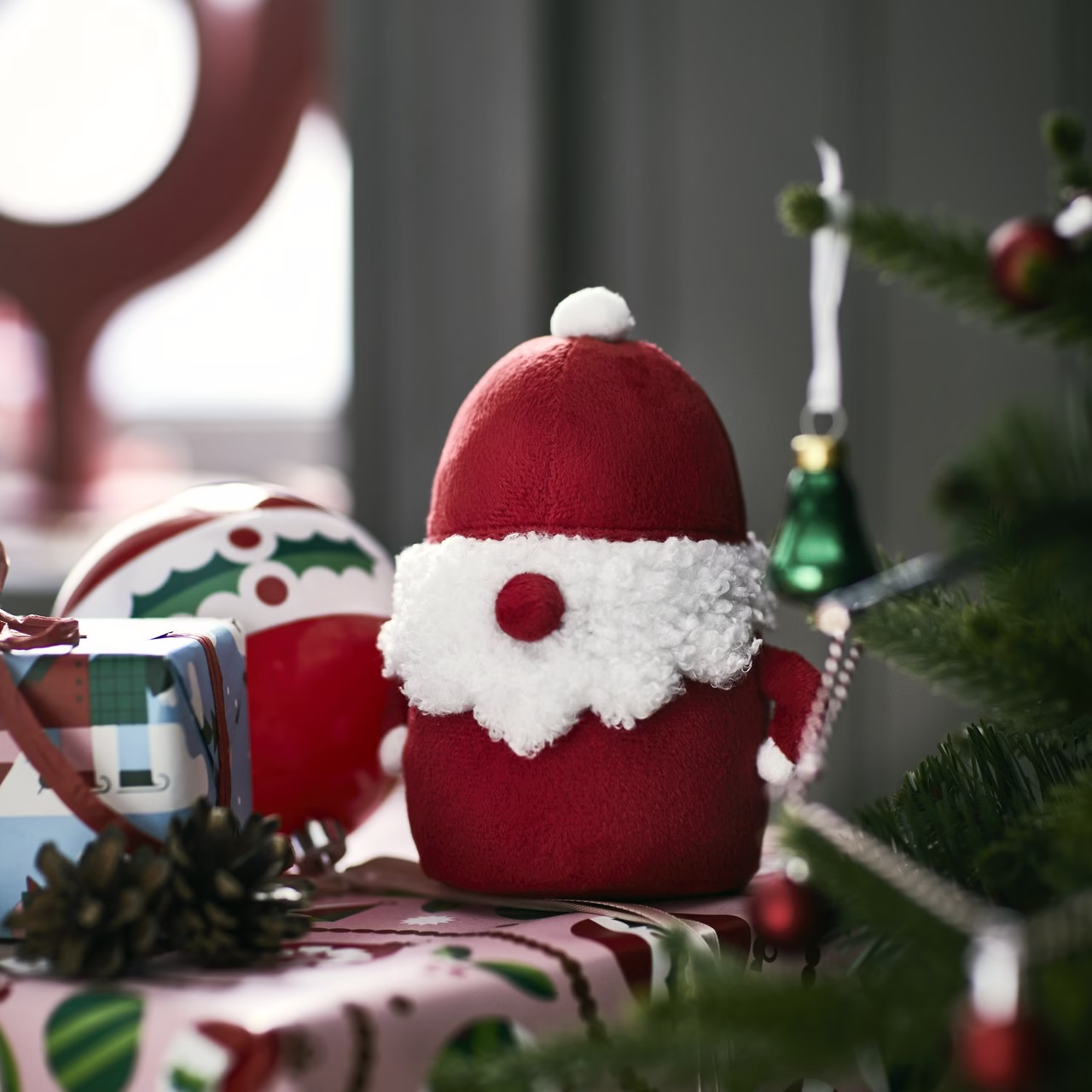Czerwona pluszowa zabawka Mikołaja obok udekorowanej choinki i prezentów.
