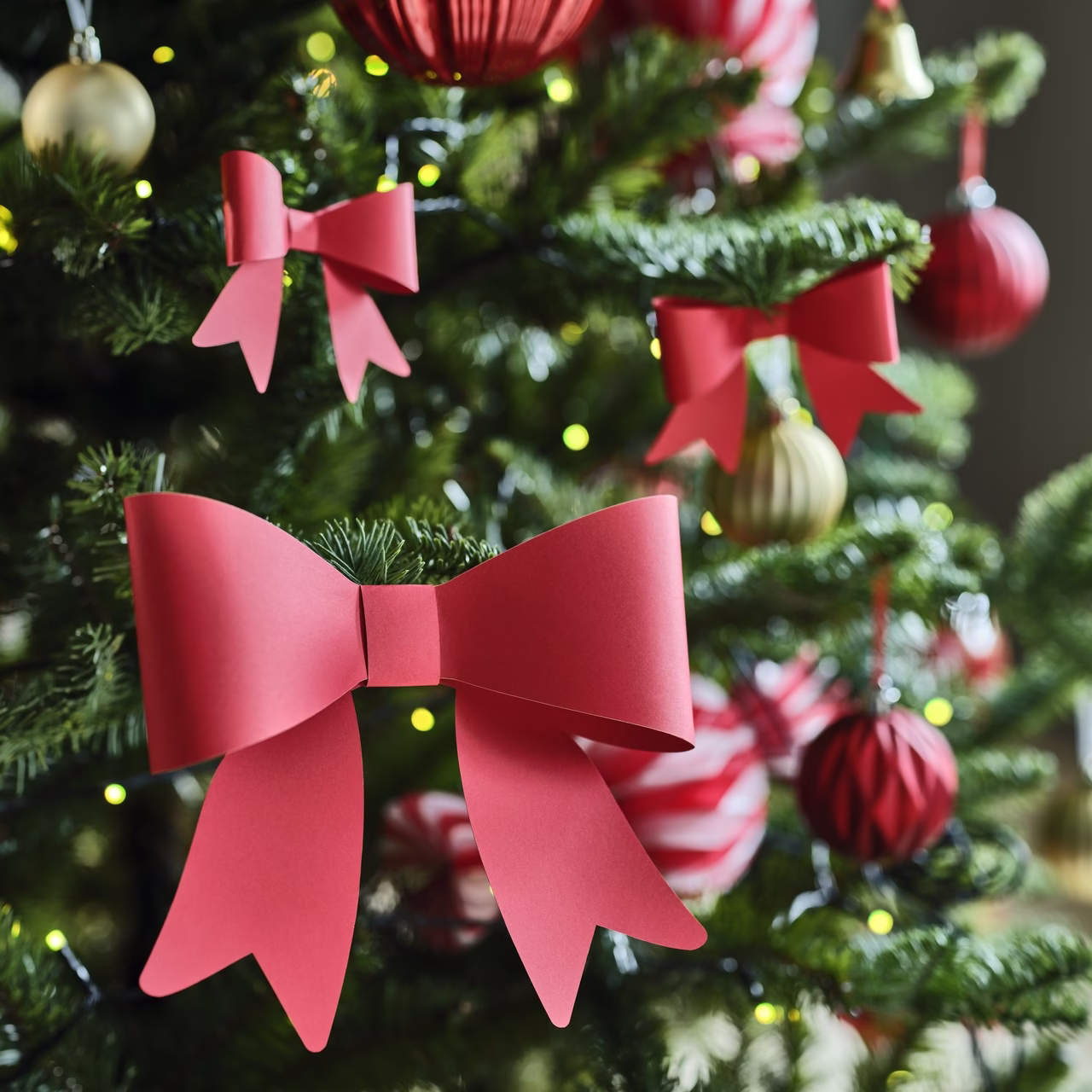 Czerwone kokardy i złote bombki na choince z zielonymi gałązkami.