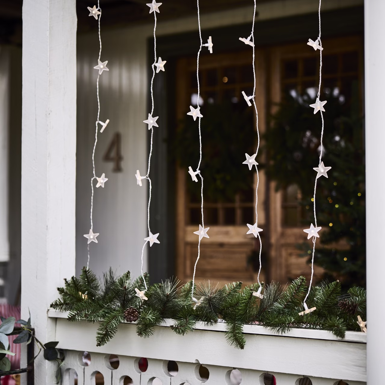 Świąteczne lampki w kształcie gwiazdek ozdabiają białą werandę z zielonymi gałązkami.