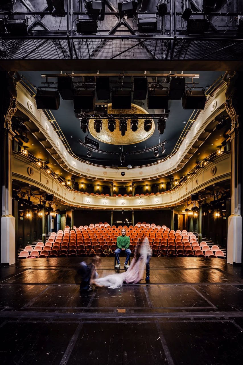 Zabytkowe wnętrze teatru z czerwonymi krzesłami i złotym sufitem.