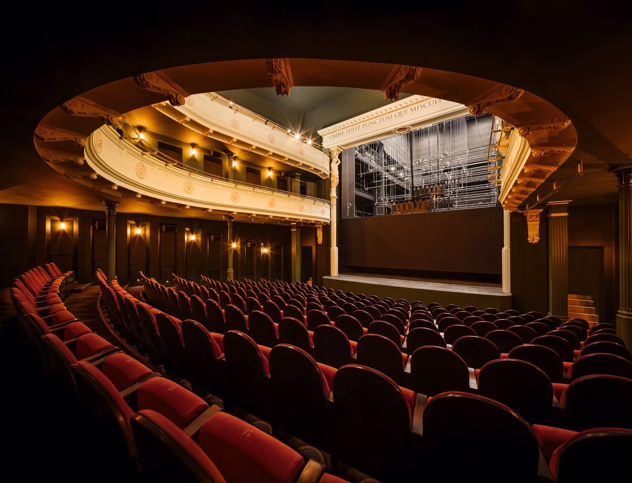 Luksusowe wnętrze teatru z balkonami i czerwonymi fotelami.