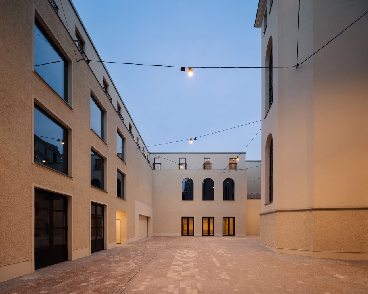 Nowoczesne podwórze z gładkimi elewacjami, szklane okna, zawieszone lampki.