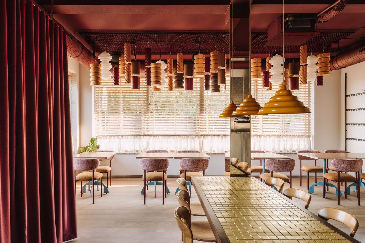 Wnętrze restauracji z drewnianymi żaluzjami, czerwonymi zasłonami i unikalnymi lampami.