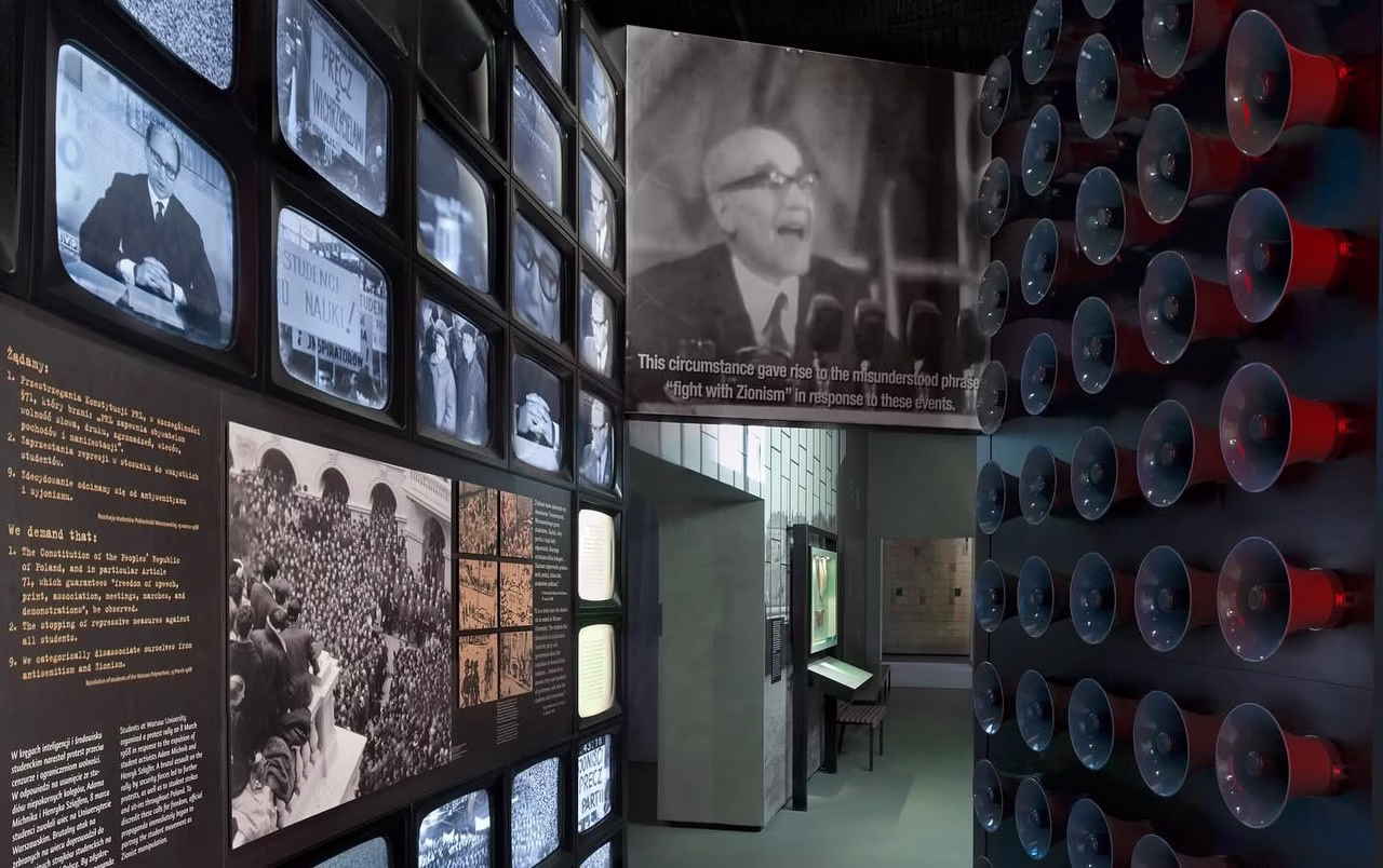 Wystawa historyczna z telewizorami i głośnikami, czarno-białe fotografie.