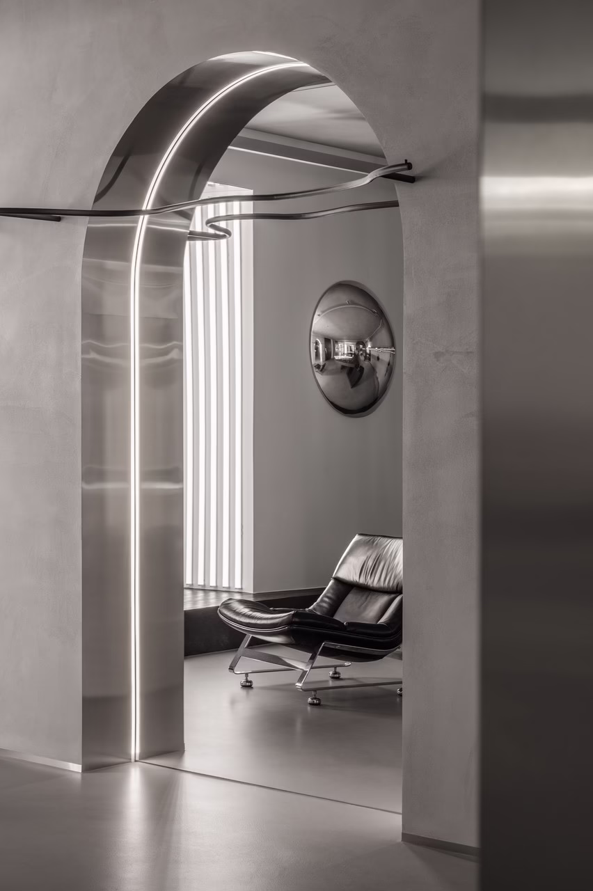 Nowoczesne wnętrze z metalowym łukiem, skórzanym fotelem i lustrzaną dekoracją.