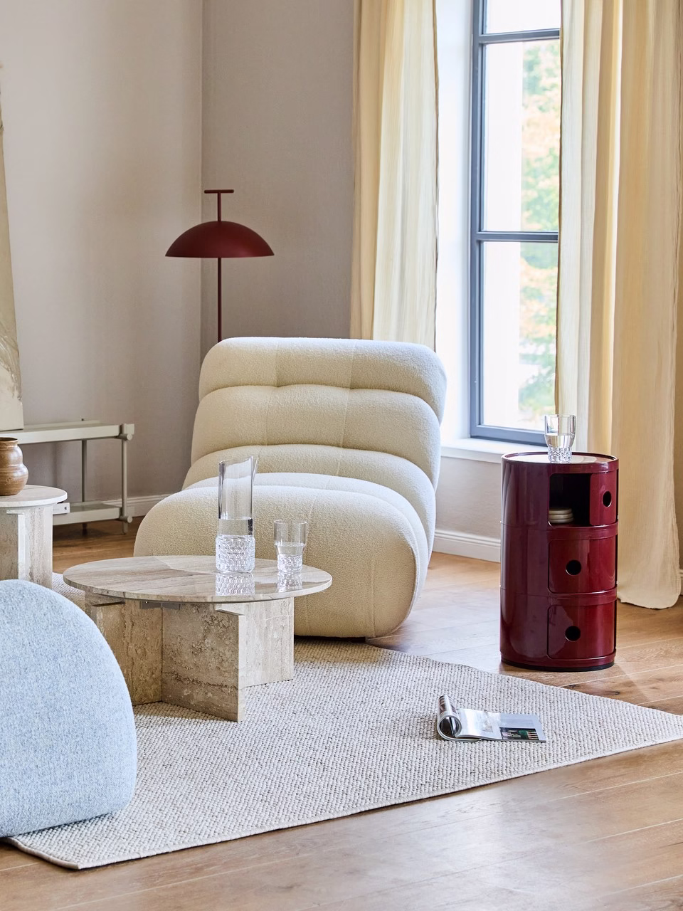 Jasny salon z beżową sofą, trawertynowym stolikiem i bordową lampą.