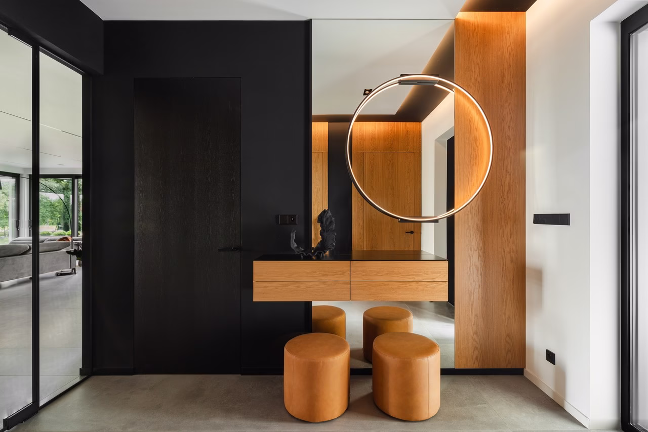 Nowoczesna łazienka z okrągłym lustrem, drewnianymi szafkami, czarne ściany.