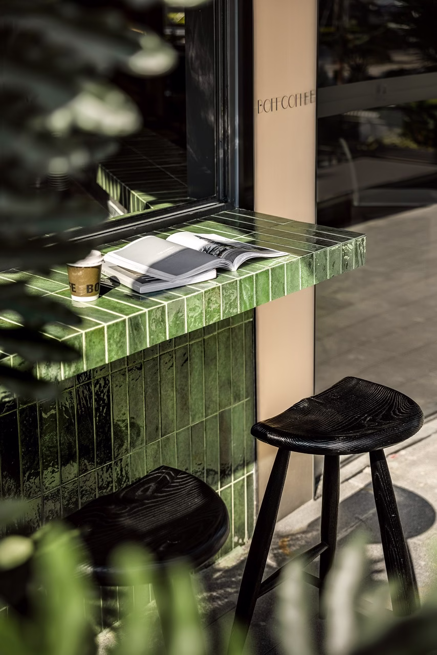 Wnętrze kawiarni z zielonym blatem, drewnianymi stołkami i książką.