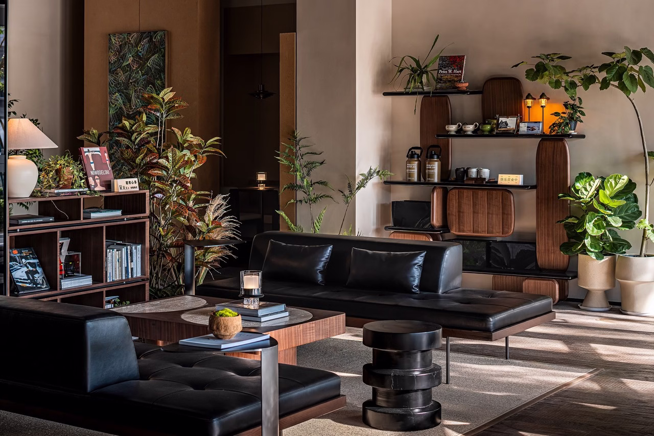 Nowoczesny salon z czarnymi skórzanymi sofami, drewnianymi półkami i roślinami.