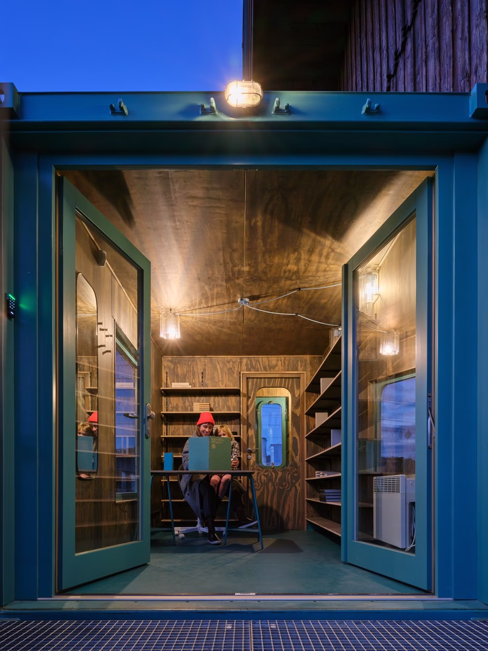 Nowoczesne biuro w kontenerze z drewnianymi półkami i dużymi drzwiami.