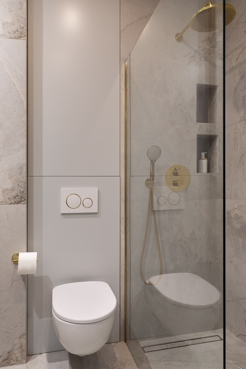 Łazienka z marmurowymi ścianami, złotą armaturą i prysznicem ze szkła.