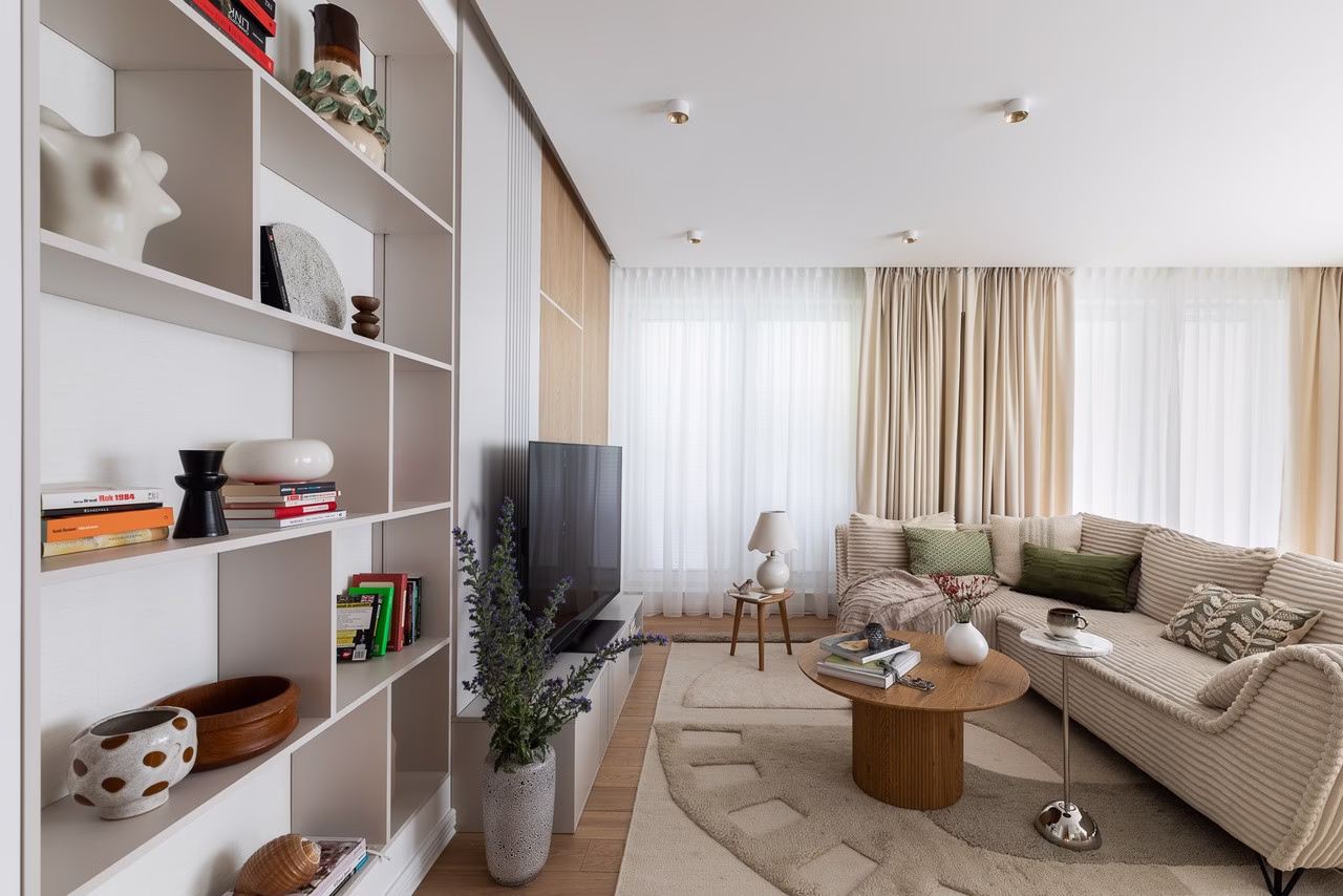 Elegancki salon z beżową sofą, drewnianym stolikiem i regałem.