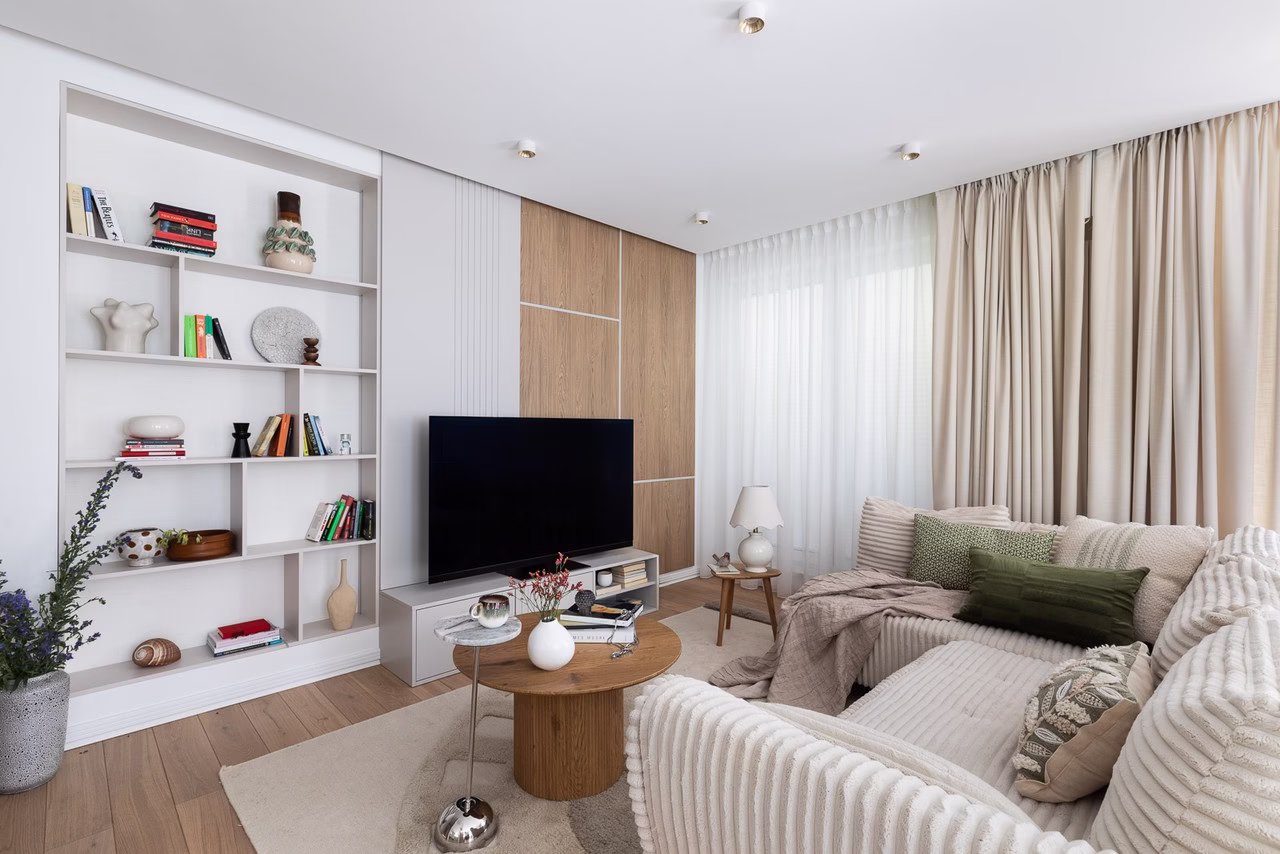 Jasny salon z beżową sofą, zielonymi poduszkami i drewnianym stolikiem.