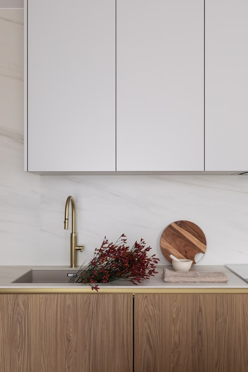 Nowoczesna kuchnia z drewnianymi szafkami, złotym kranem i białą ścianą.