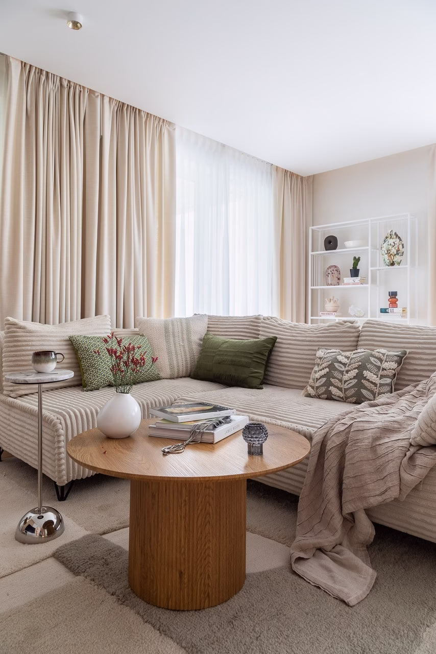 Elegancki salon z beżową kanapą, zielonymi poduszkami i okrągłym stolikiem.