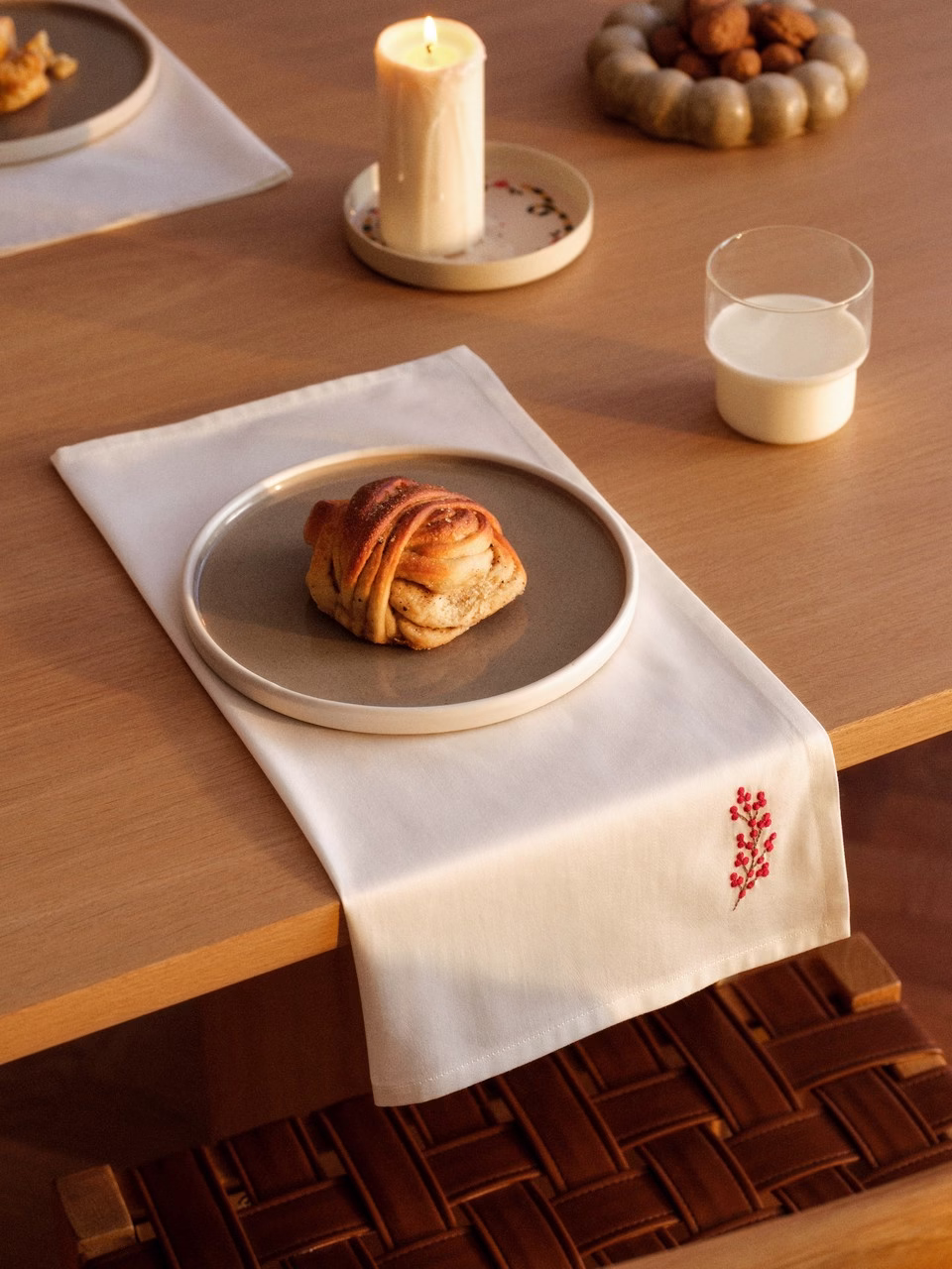 Drewniany stół z bułeczką cynamonową, świecą i szklanką mleka.