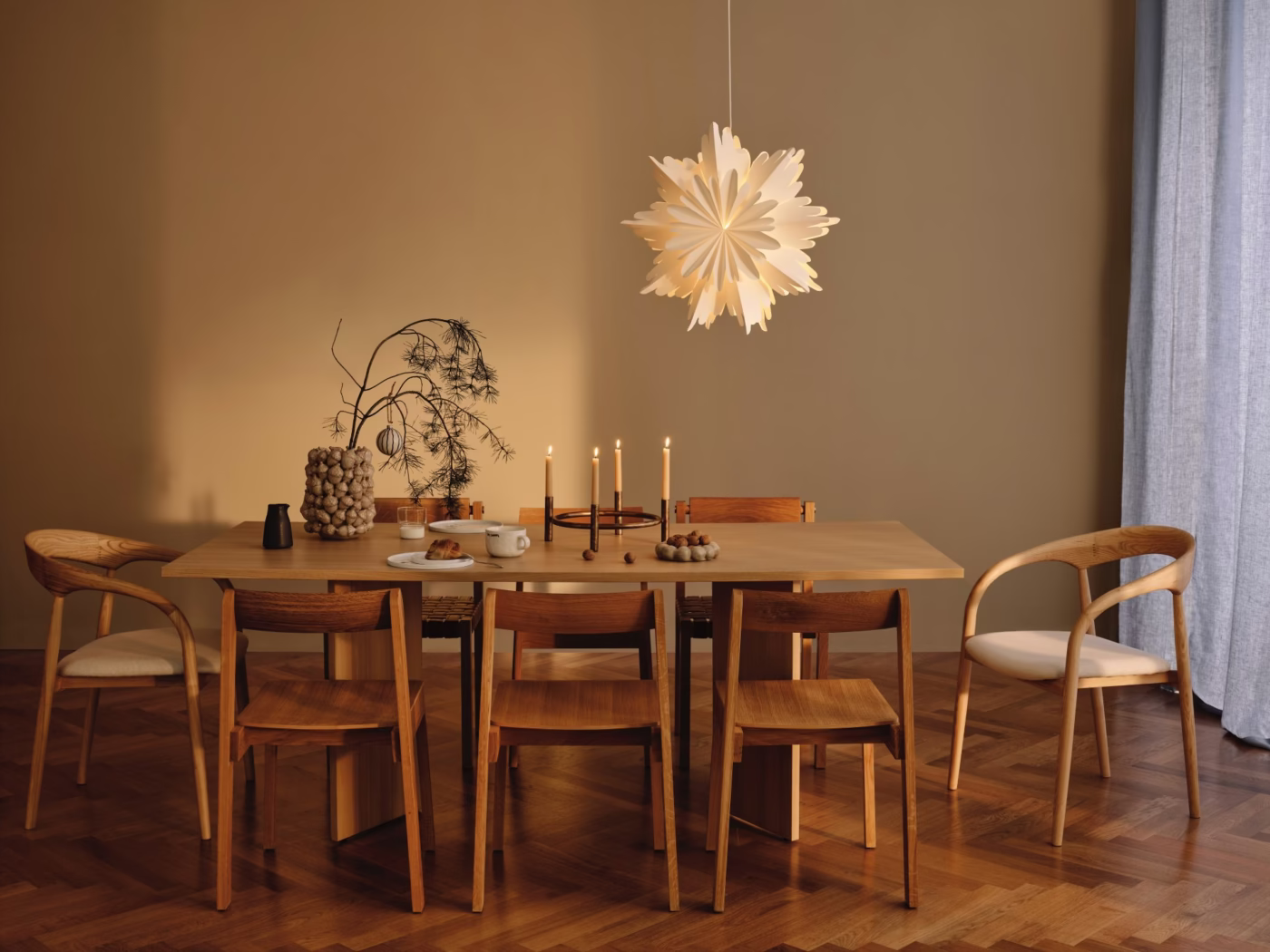 Minimalistyczna jadalnia z drewnianym stołem, designerską lampą i świecami.