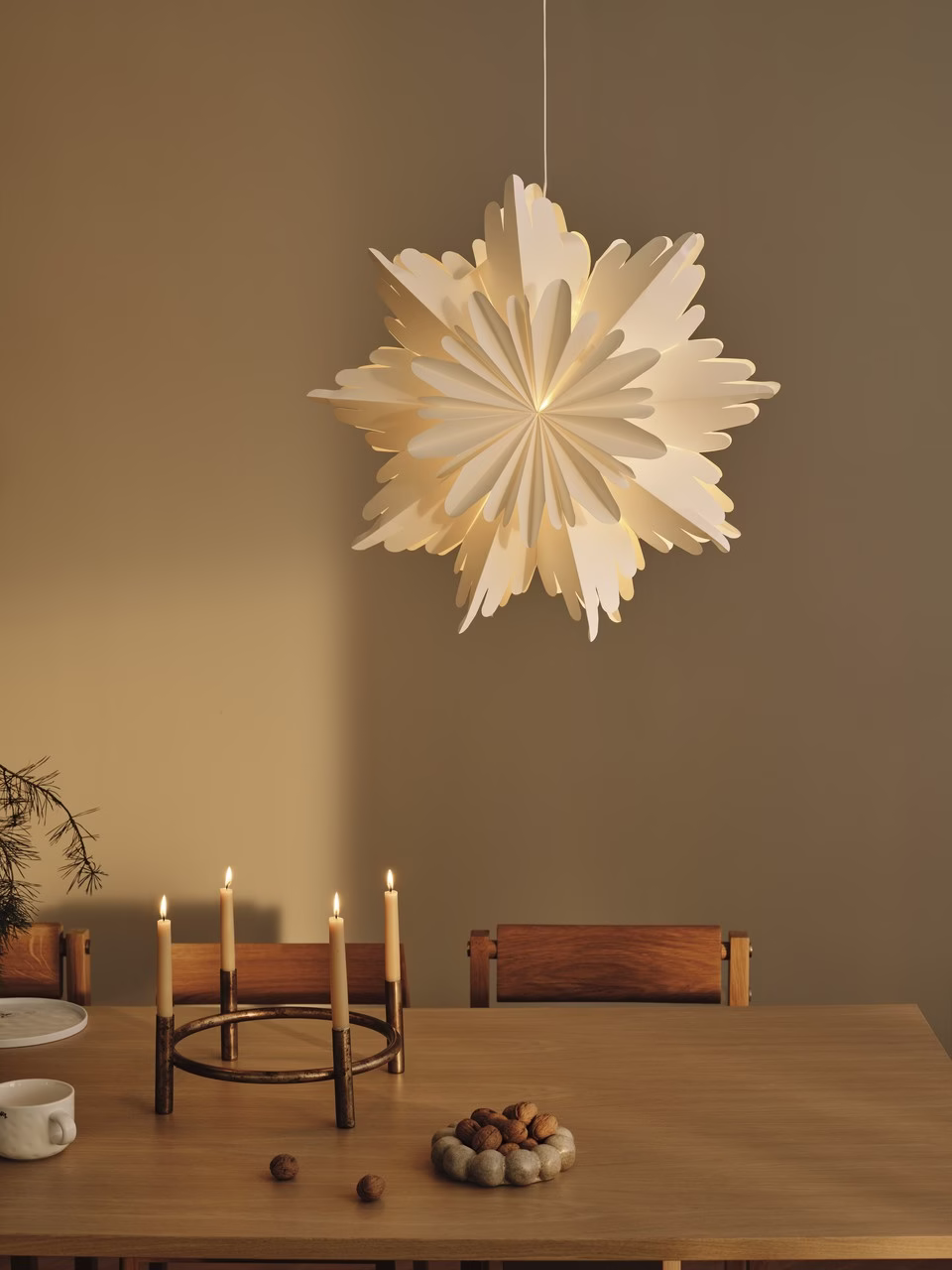 Lampion papierowy nad drewnianym stołem z orzechami i świecami.