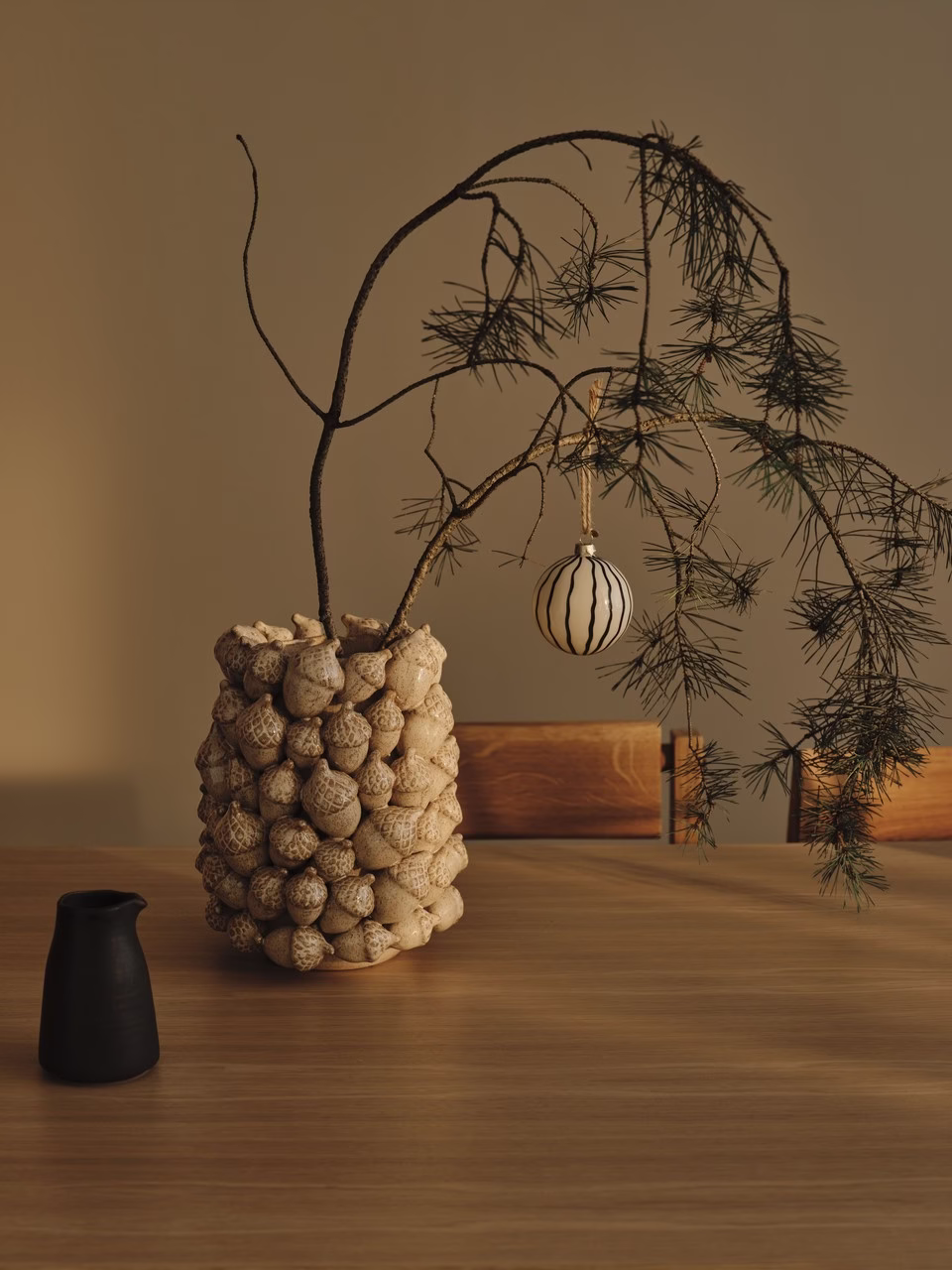 Gałązka z ozdobą w ceramicznym wazonie na drewnianym stole.