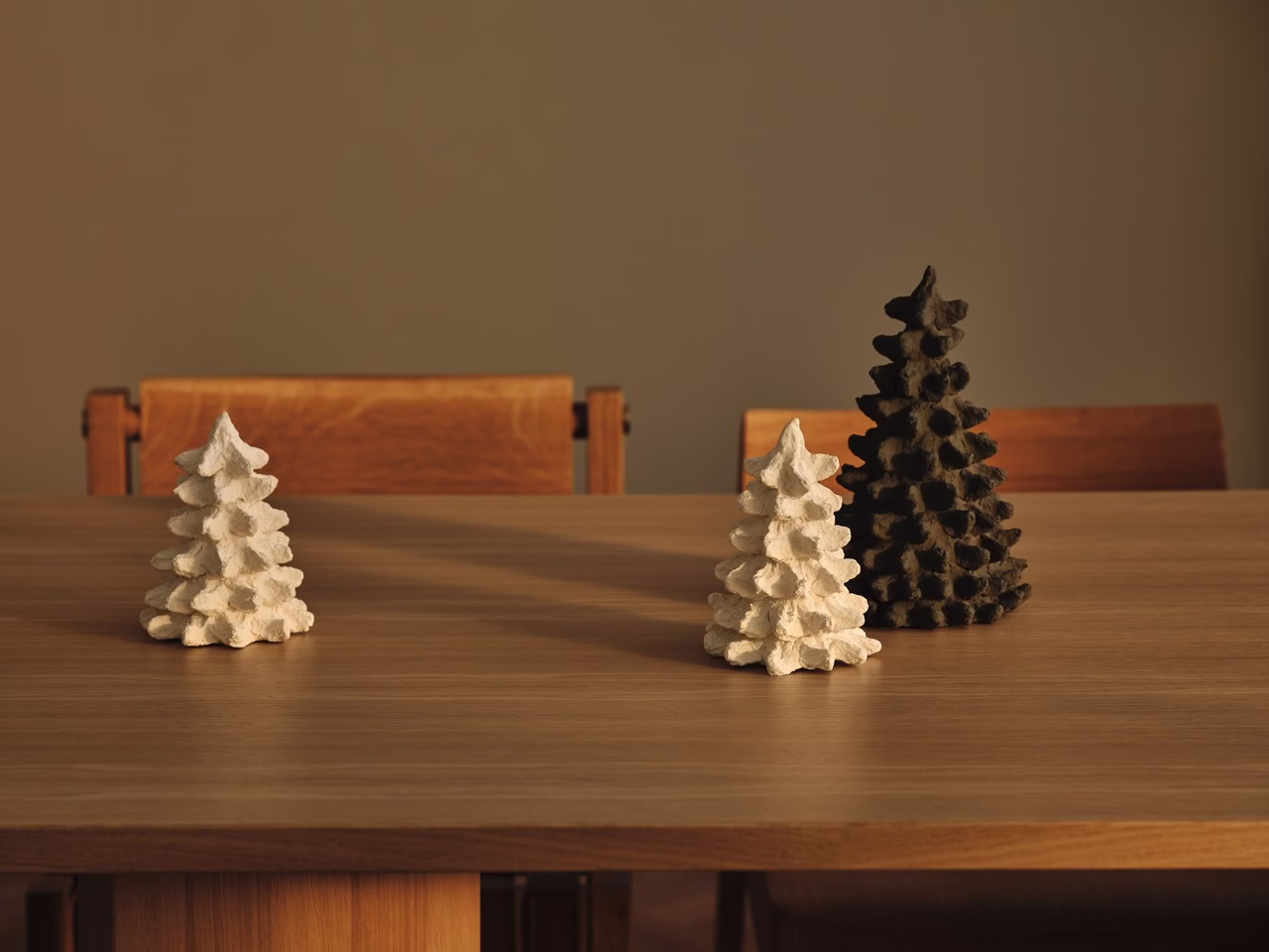 Ceramiczne choinki na drewnianym stole w minimalistycznym wnętrzu.