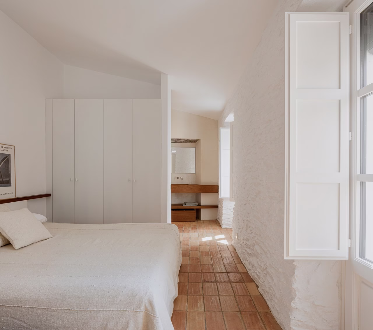 Przytulna sypialnia z białymi ścianami, drewnianą podłogą i dużym oknem.